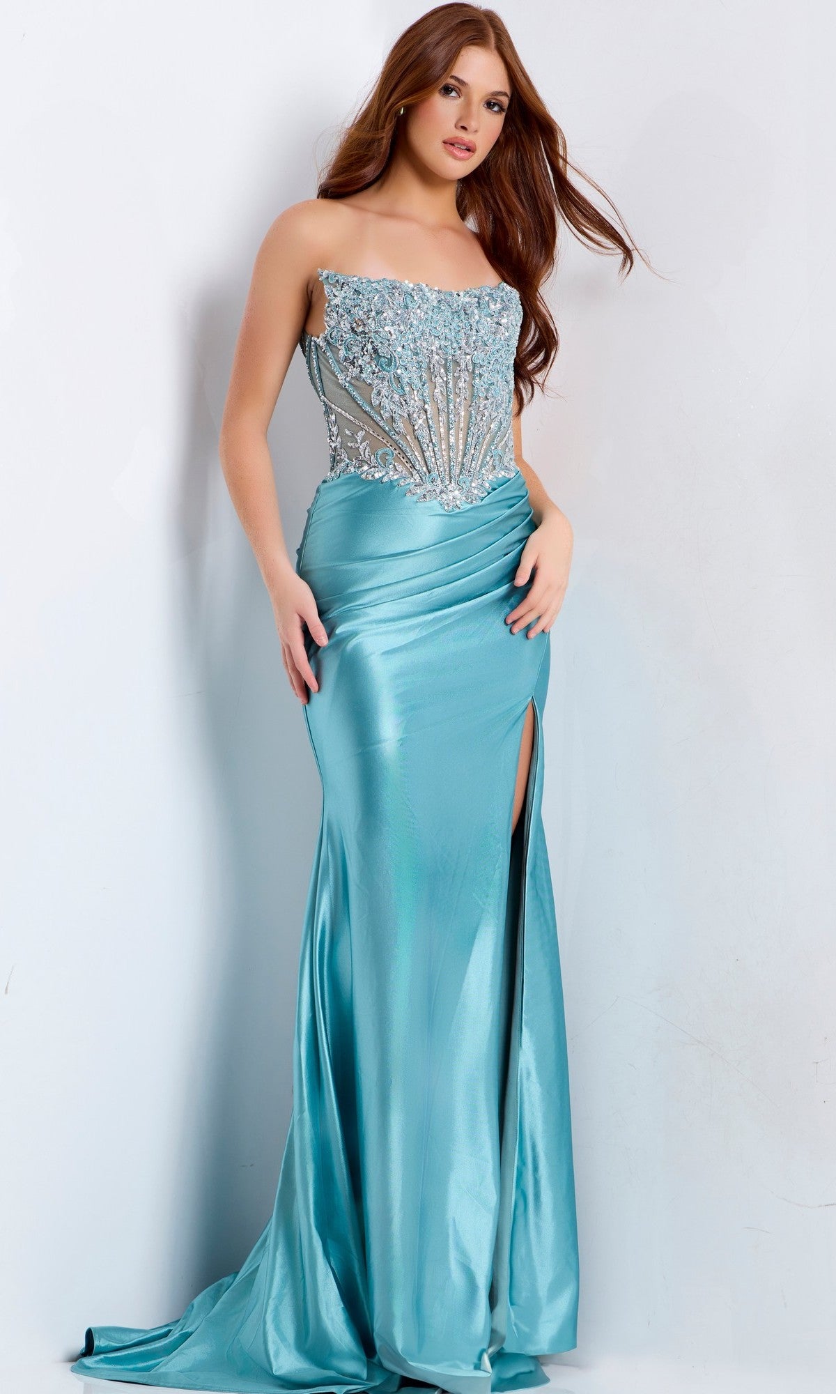 A woman wears the Jovani 49721 long prom dress in teal, featuring a strapless beaded corset bodice and a high slit in the sleek floor-length column skirt.